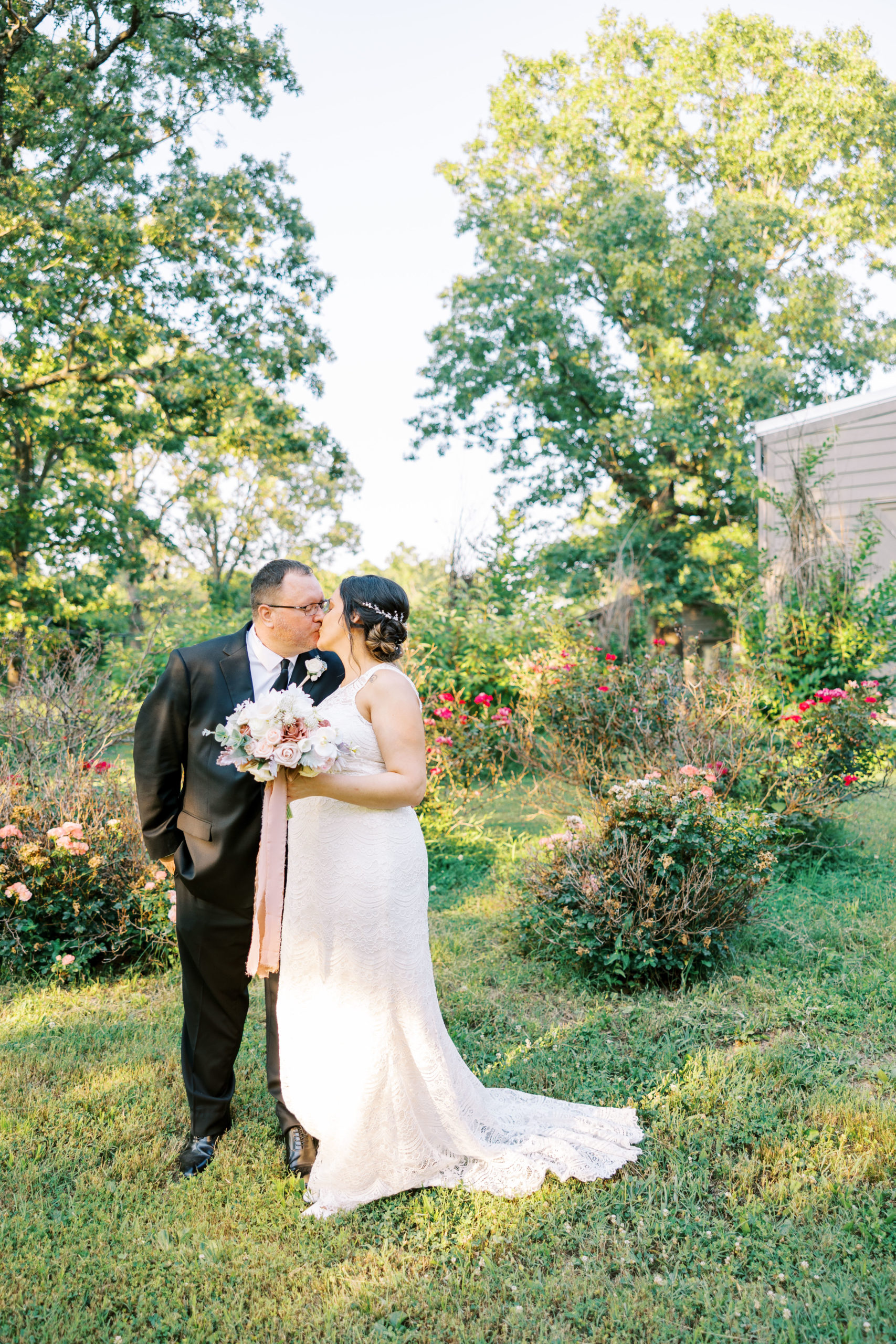 bride and groom kiss in front of rose bushes