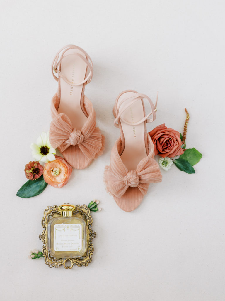 bridal shoe flat lay, including perfume and clay-colored Loeffler Randall heels