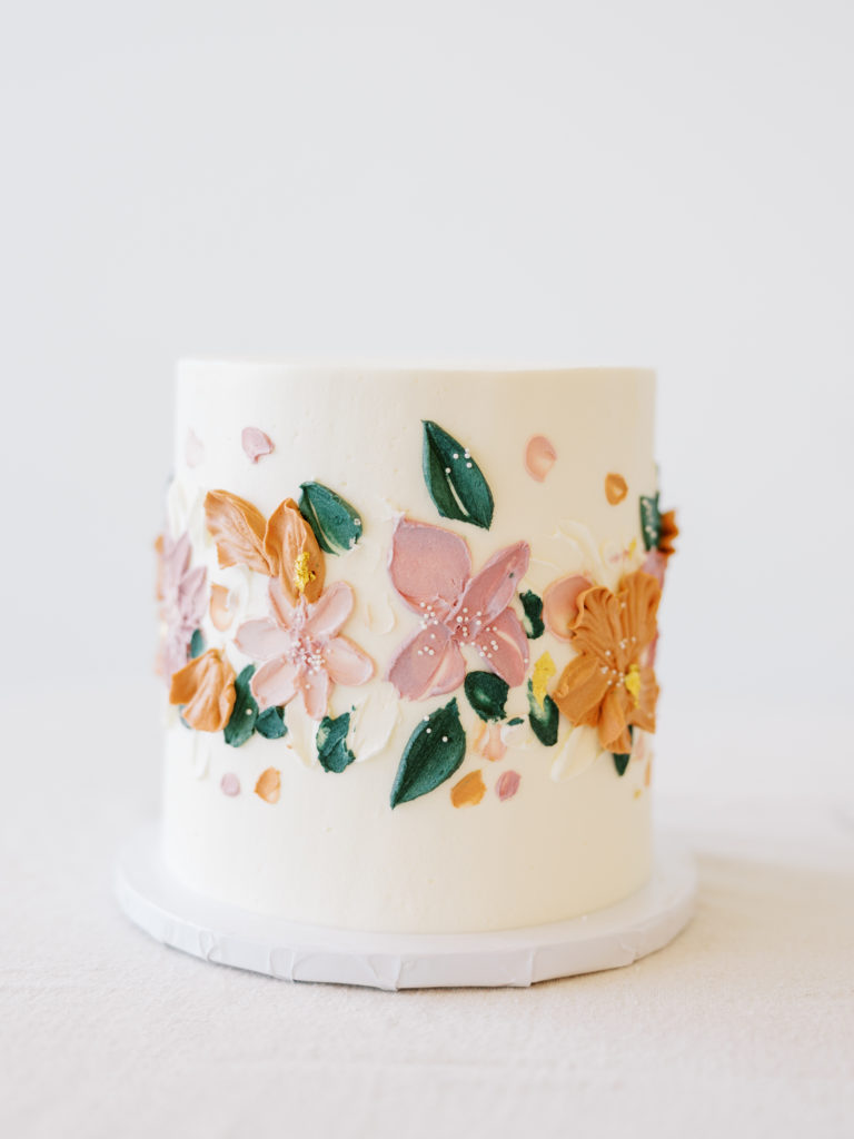 wedding cake with pink, orange, and green florals painted in buttercream