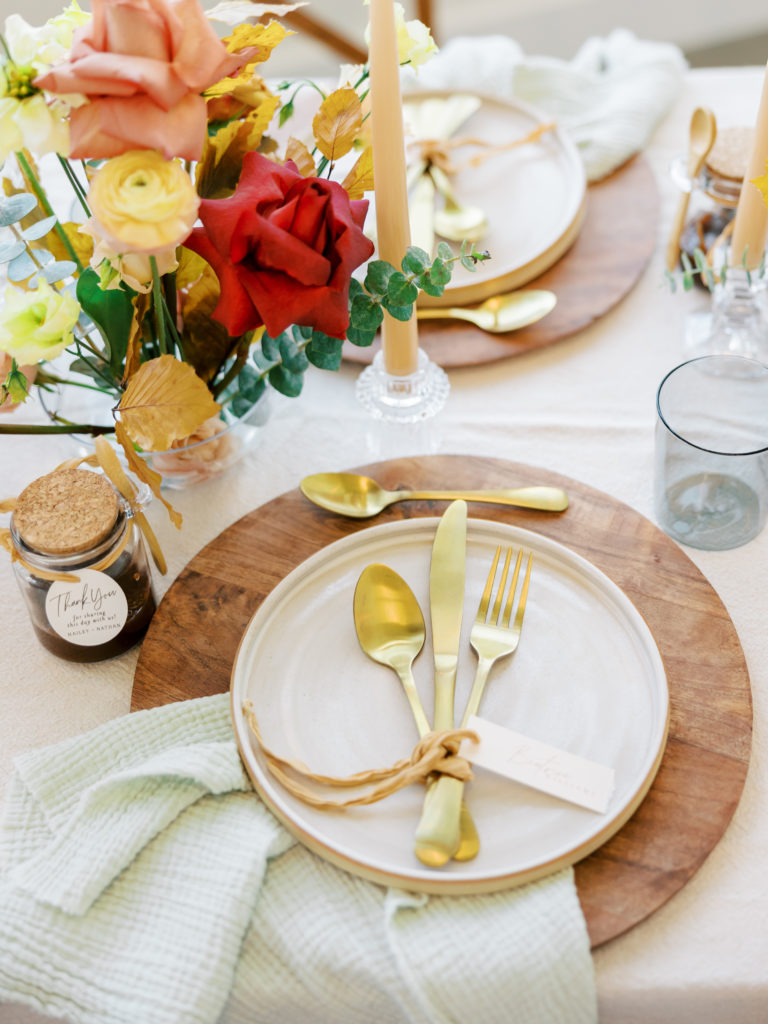 picture of table place setting with wood charger, stone plate, gold silverware, and fall florals